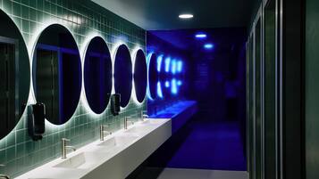 Een moderne badkamer met meerdere wastafels, verlichte spiegels en een blauw verlichte gang.