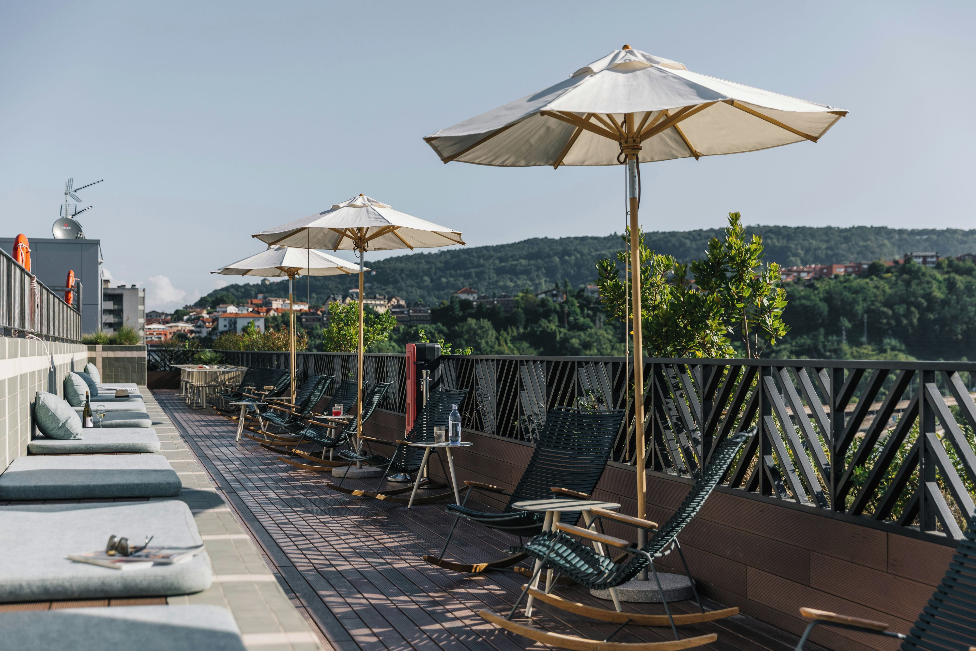 Una terraza en la azotea con mobiliario exterior, sombrillas y vistas a un paisaje montañoso.