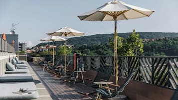 Una terraza en la azotea con mobiliario exterior, sombrillas y vistas a un paisaje montañoso.
