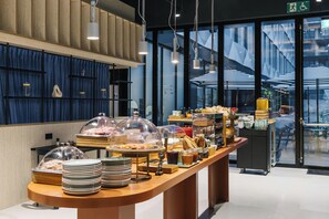 A buffet with various food items and a view of the outside through large windows. - The Social Hub San Sebastián (San Sebastián)