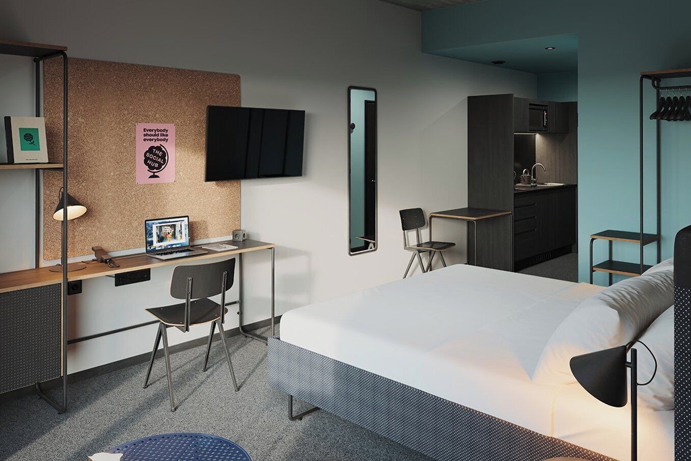 A modern hotel room with a bed, desk, chair, and a kitchenette.