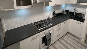 Eine moderne Küche mit weißen Schränken, einer schwarzen Arbeitsplatte, einer Edelstahl-Dunstabzugshaube und einem Gasherd.