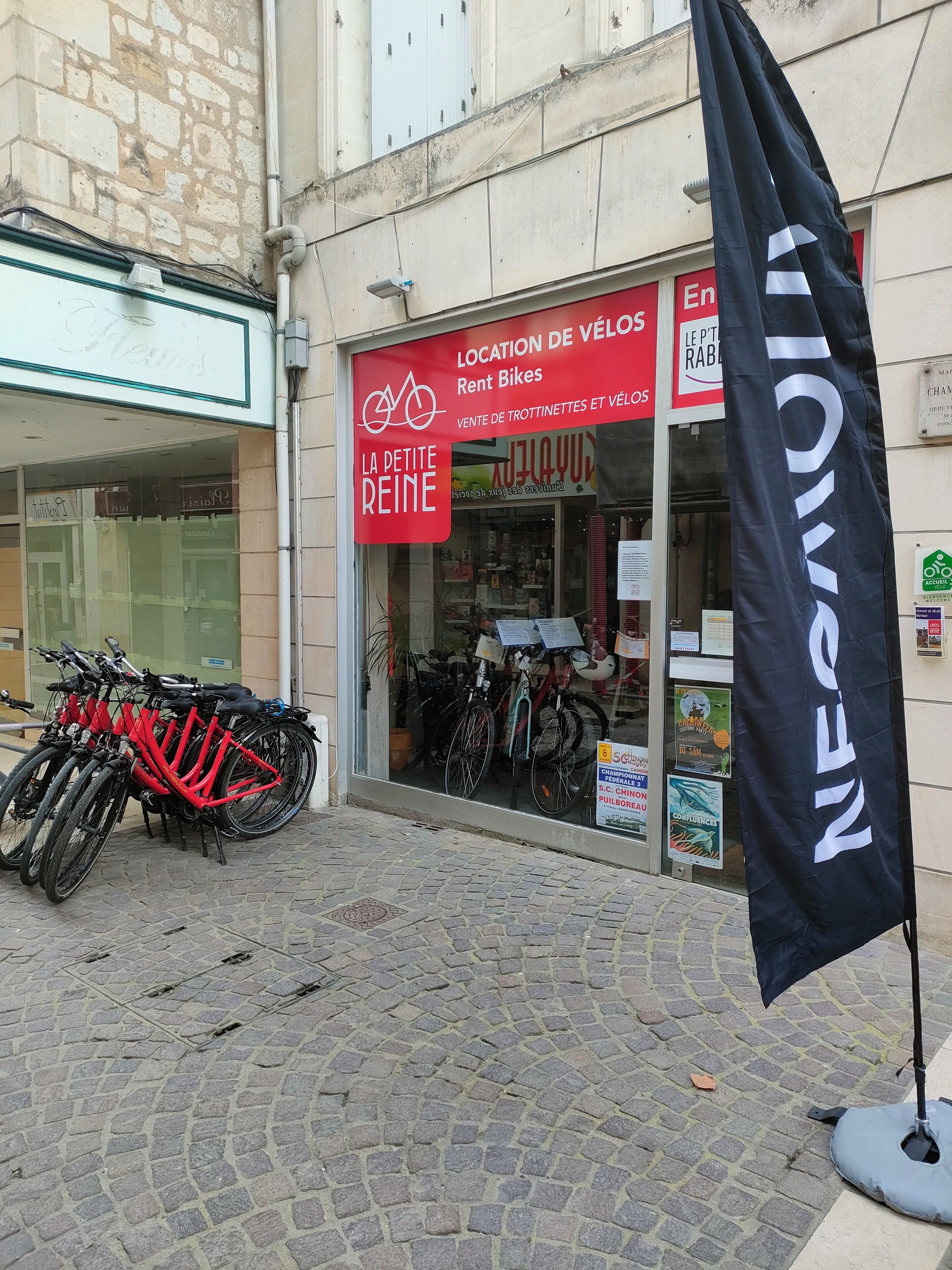 Une devanture de magasin avec une enseigne rouge indiquant la location et la vente de vélos. Plusieurs vélos sont garés à l’extérieur.