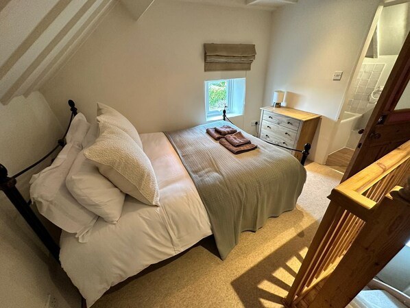 A bedroom with a bed, pillows, a window, a nightstand, and a wooden staircase.