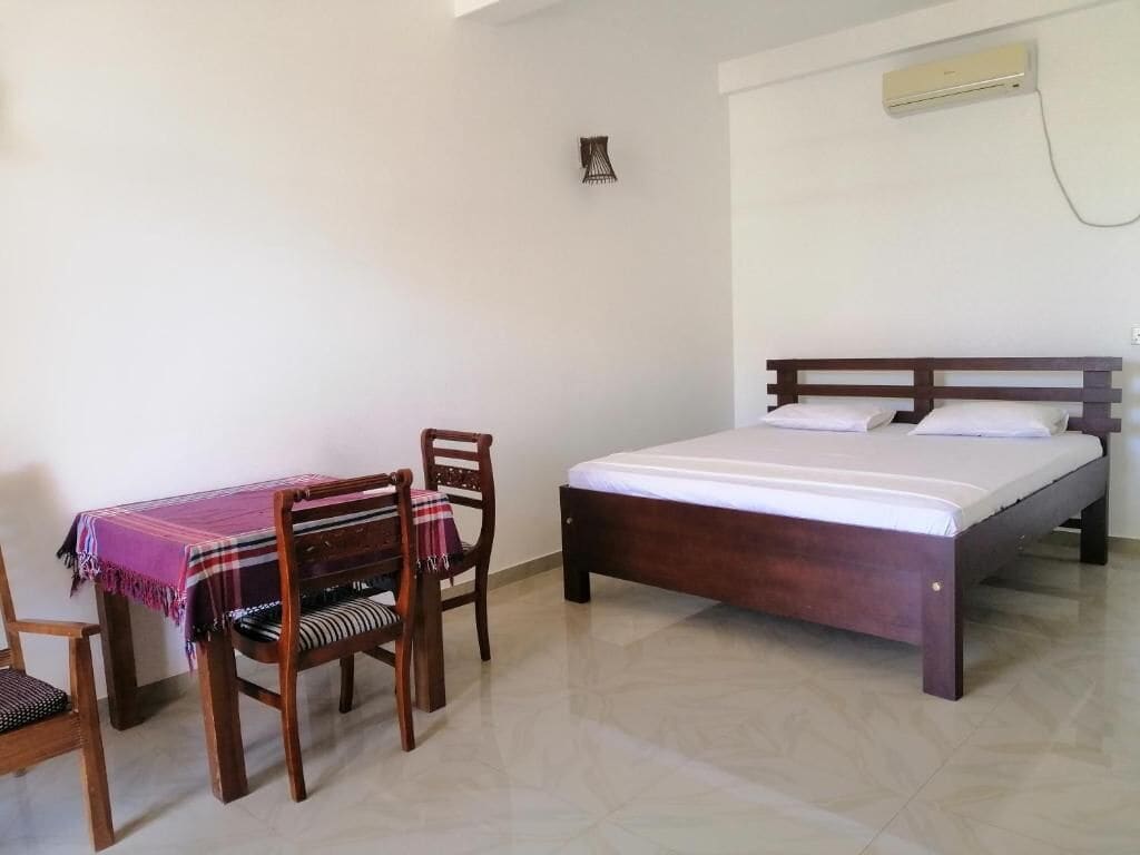 Un dormitorio con cama, una silla, una mesa y un aire acondicionado instalado en la pared.