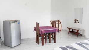 A small, clean room with a refrigerator, a dining table with chairs, a bench, and a mirror on the wall. - Beluga Sands Beach (Ambalangoda)