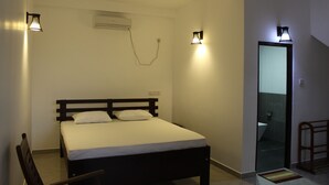 A bedroom with a bed, bedside lamps, an air conditioning unit, and a door leading to a bathroom. - Beluga Sands Beach (Ambalangoda)