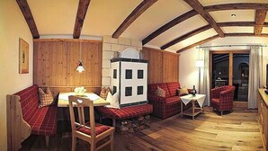 Une pièce chaleureuse avec des poutres apparentes, une cheminée, une table à manger avec des bancs et un canapé.
