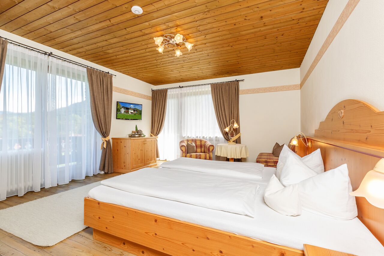 Une chambre avec un lit en bois, un plafond en bois et une vue sur un jardin, visible à travers de grandes fenêtres.