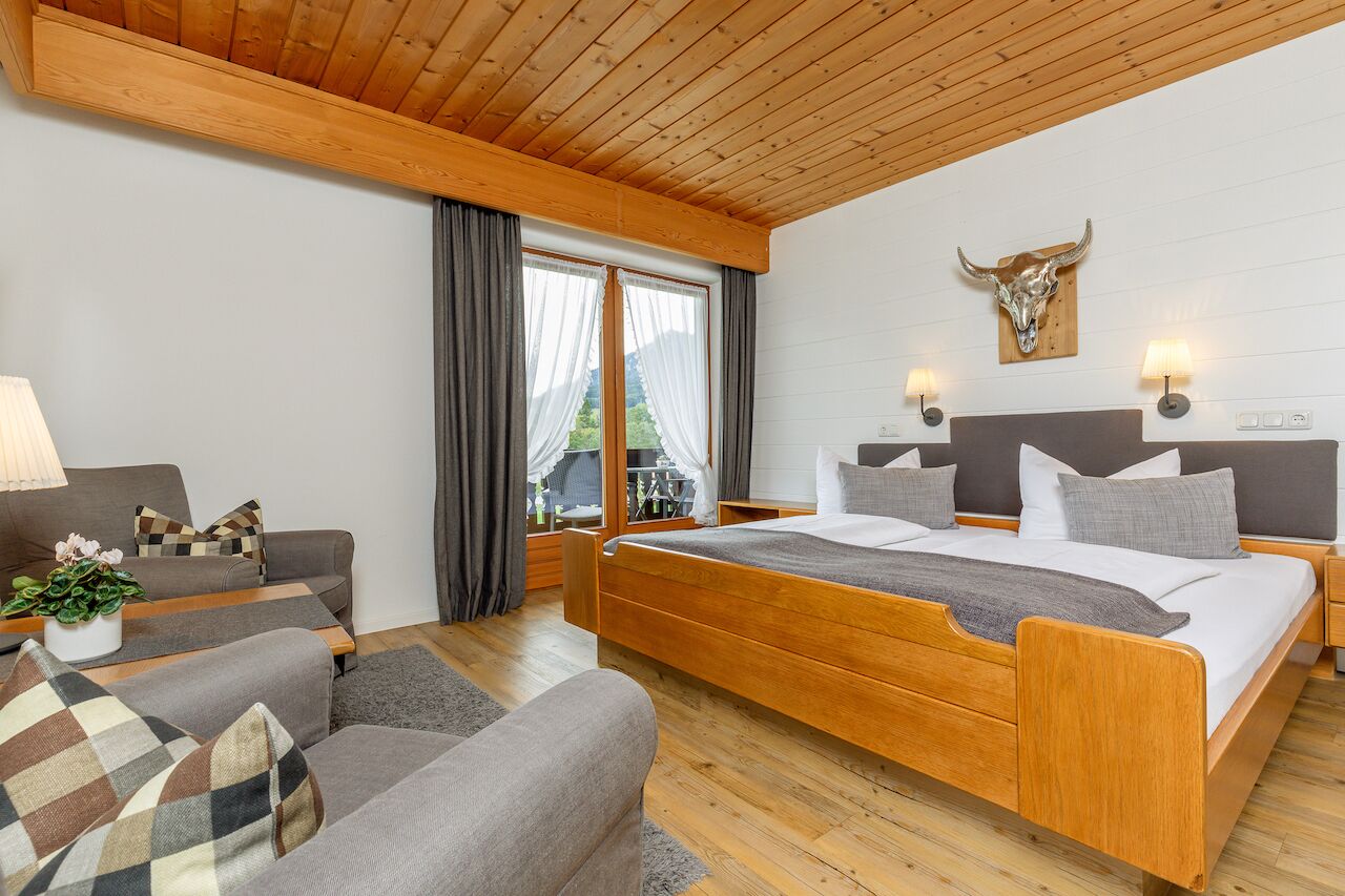 Ett sovrum med en säng i trä, en soffa, ett skrivbord och en lampa.
