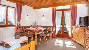 A cozy room with a wooden ceiling, a dining table with chairs, a bench, a television, and a window with curtains.