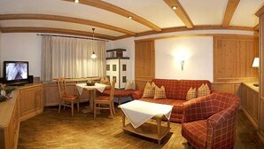 A cozy living room with a wooden ceiling, a red plaid sofa, a wooden coffee table, and a television on a wooden cabinet. - Fewo Sonntagshorn Terrasse, Küche, 1 Schlaf- und 1 Wohn-/schlafz., max 5 Pers (Ruhpolding)