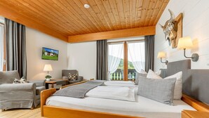 A bedroom with a wooden ceiling, a bed with white linens, a grey sofa, a small table with a lamp, and a wall-mounted lamp. - Fewo Sonntagshorn Terrasse, Küche, 1 Schlaf- und 1 Wohn-/schlafz., max 5 Pers (Ruhpolding)