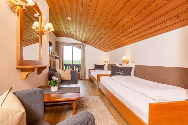 A cozy room with a wooden ceiling, a sofa, a small table, a bed, and a window with curtains.