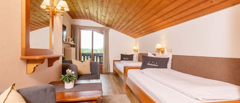 A cozy room with a wooden ceiling, a sofa, a small table, a bed, and a window with curtains.