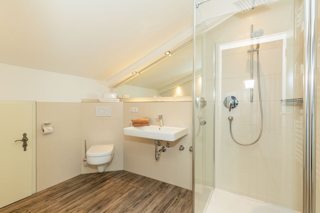 A modern bathroom with a wooden floor, a white sink, a toilet, and a glass-enclosed shower.