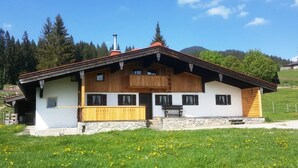 Un chalet traditionnel en bois, doté de fondations en pierre, d’un balcon en bois et d’un escalier en pierre menant à l’entrée.