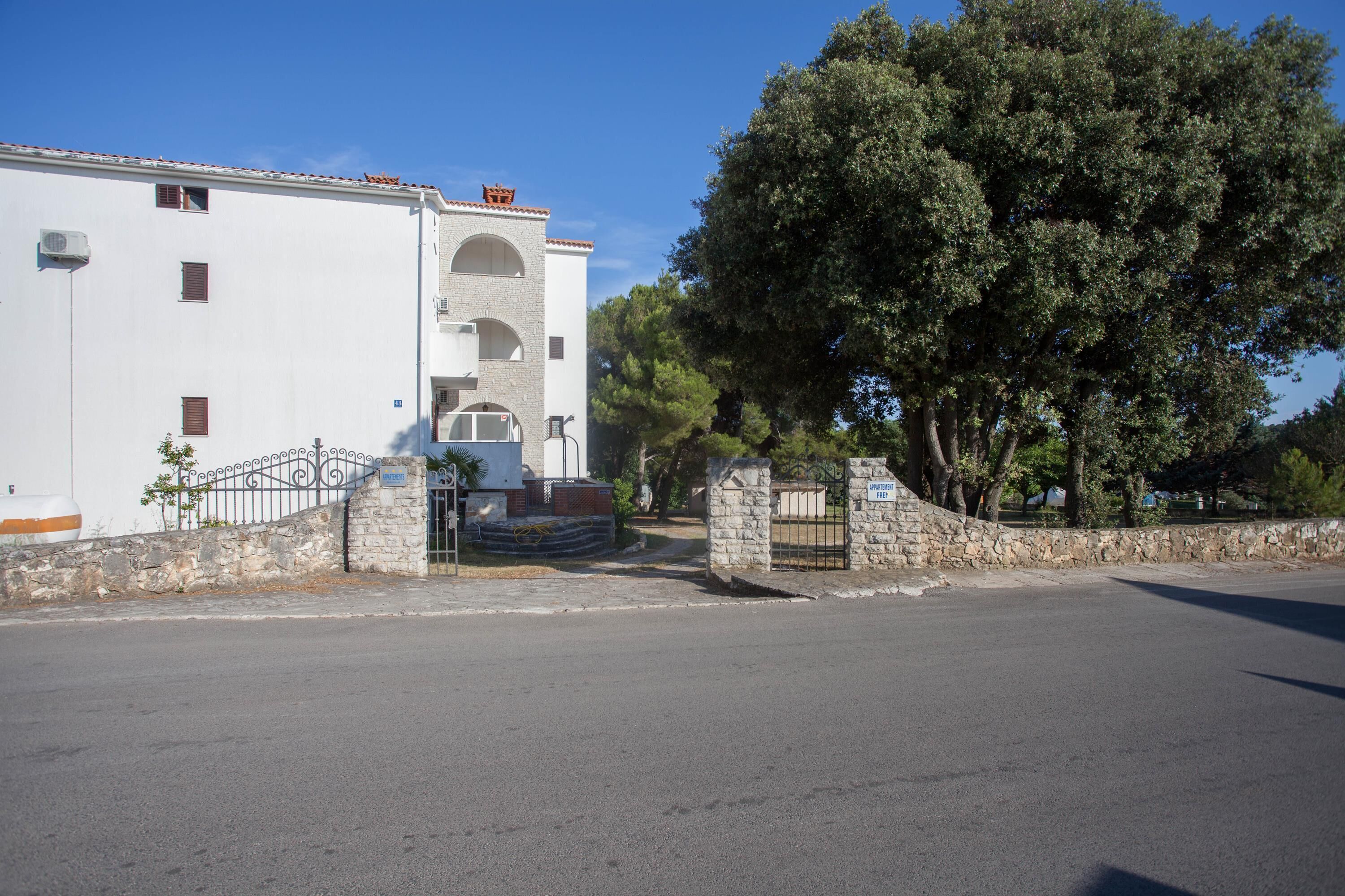 Un bâtiment blanc avec un portail d’entrée en pierre, un ciel dégagé et un grand arbre en arrière-plan.