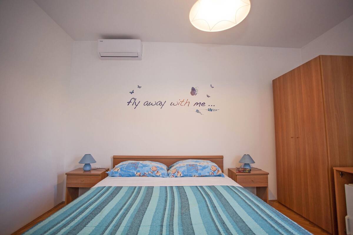 Une chambre à coucher avec un lit, deux tables de chevet avec des lampes, une armoire et un mur décoré d’un motif de papillon.