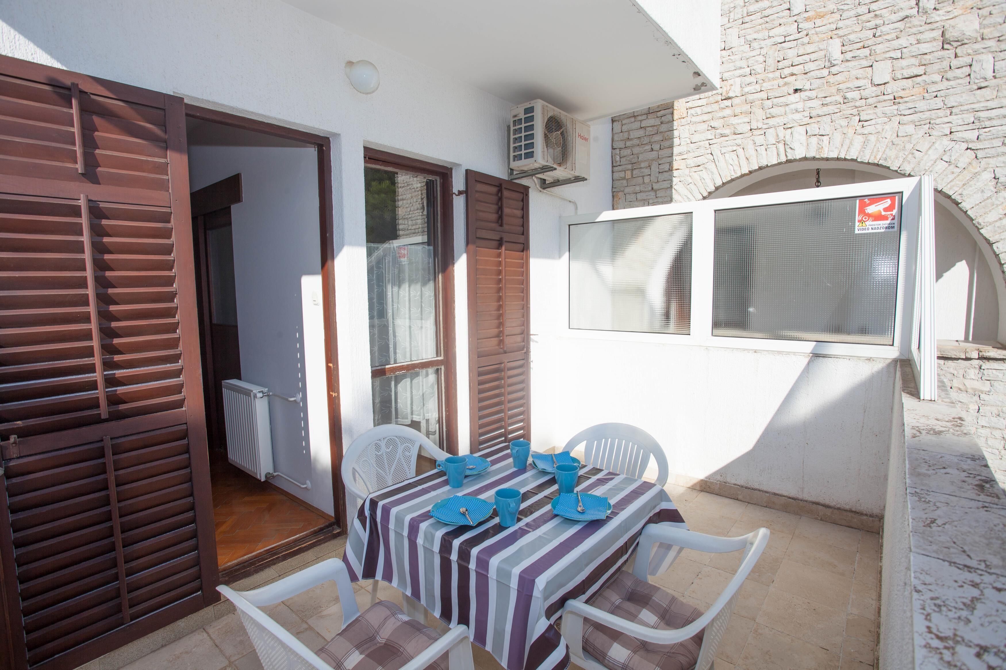 A patio with a table set for two, white chairs, and a striped tablecloth.