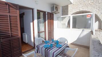Un patio con una mesa dispuesta para dos personas, sillas blancas y mantel a rayas.