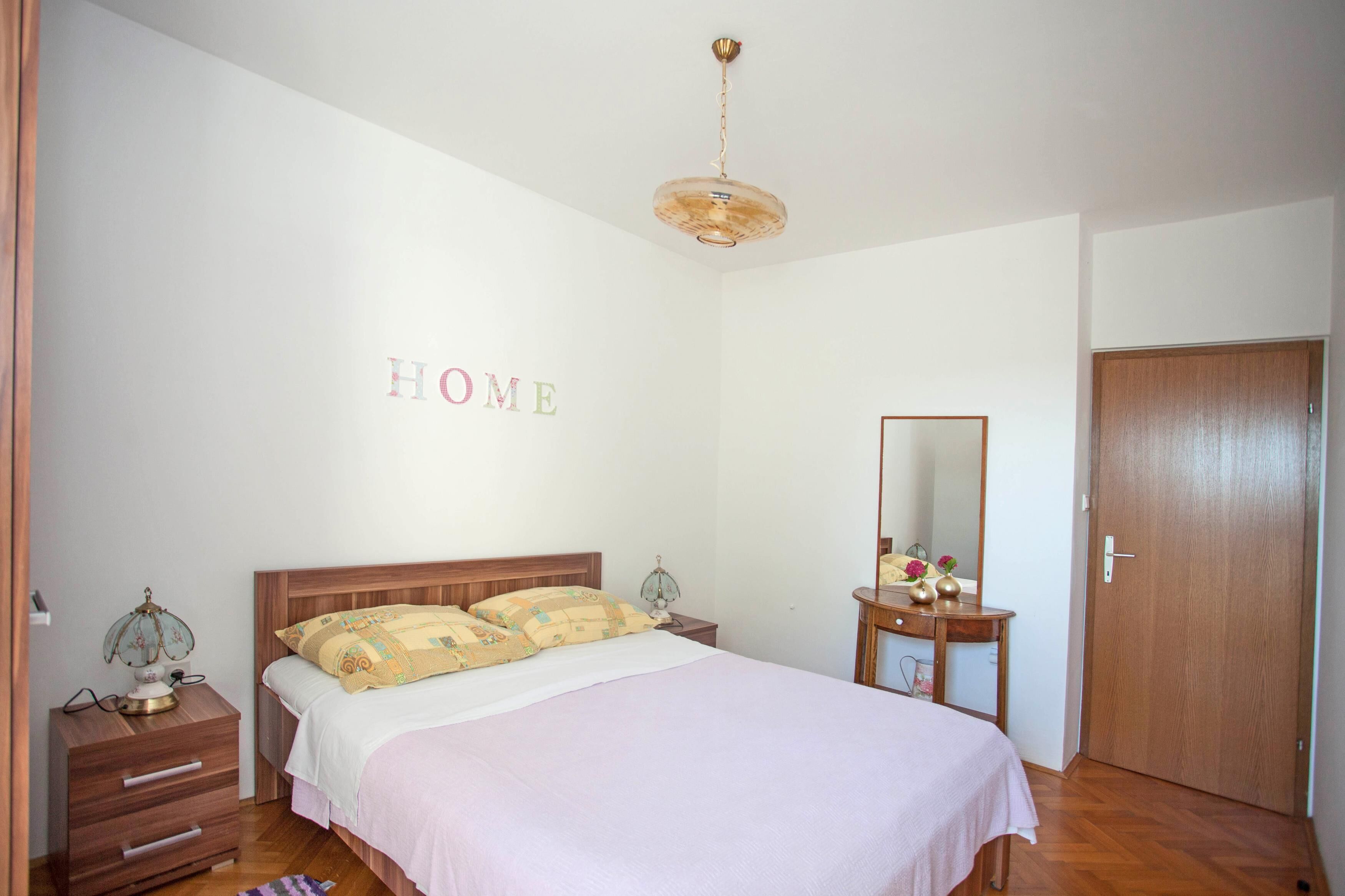 Une chambre à coucher avec un lit, une table de chevet, une commode, un miroir et une porte.