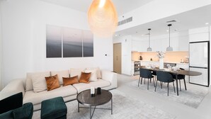A modern living room with a sofa, coffee table, and a dining area with chairs and a table. - Nasma Holiday Homes - Creek Horizon Tower 1 (Dubai)