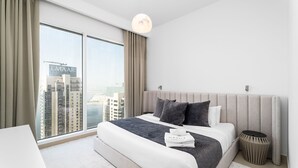 A modern hotel room with a large bed, a bedside table, a round side table, and a view of the cityscape through floor-to-ceiling windows. - Nasma Holiday Homes - Creek Horizon Tower 1 (Dubai)