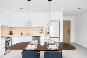 A modern kitchen with white cabinetry, a dining table set for four, and pendant lights above.