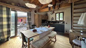A cozy kitchen with wooden beams, a dining table set for four, and a view of the outside.