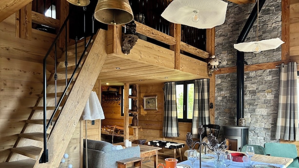 A rustic wooden interior with a dining area, a staircase, and a stone wall.