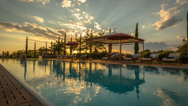 Une piscine entourée d’arbres et agrémentée de transats, de parasols et d’un belvédère.