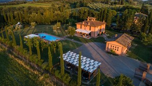 Vue aérienne d’une propriété comprenant une piscine, un abri-voiture couvert et une grande maison dotée d’un patio.