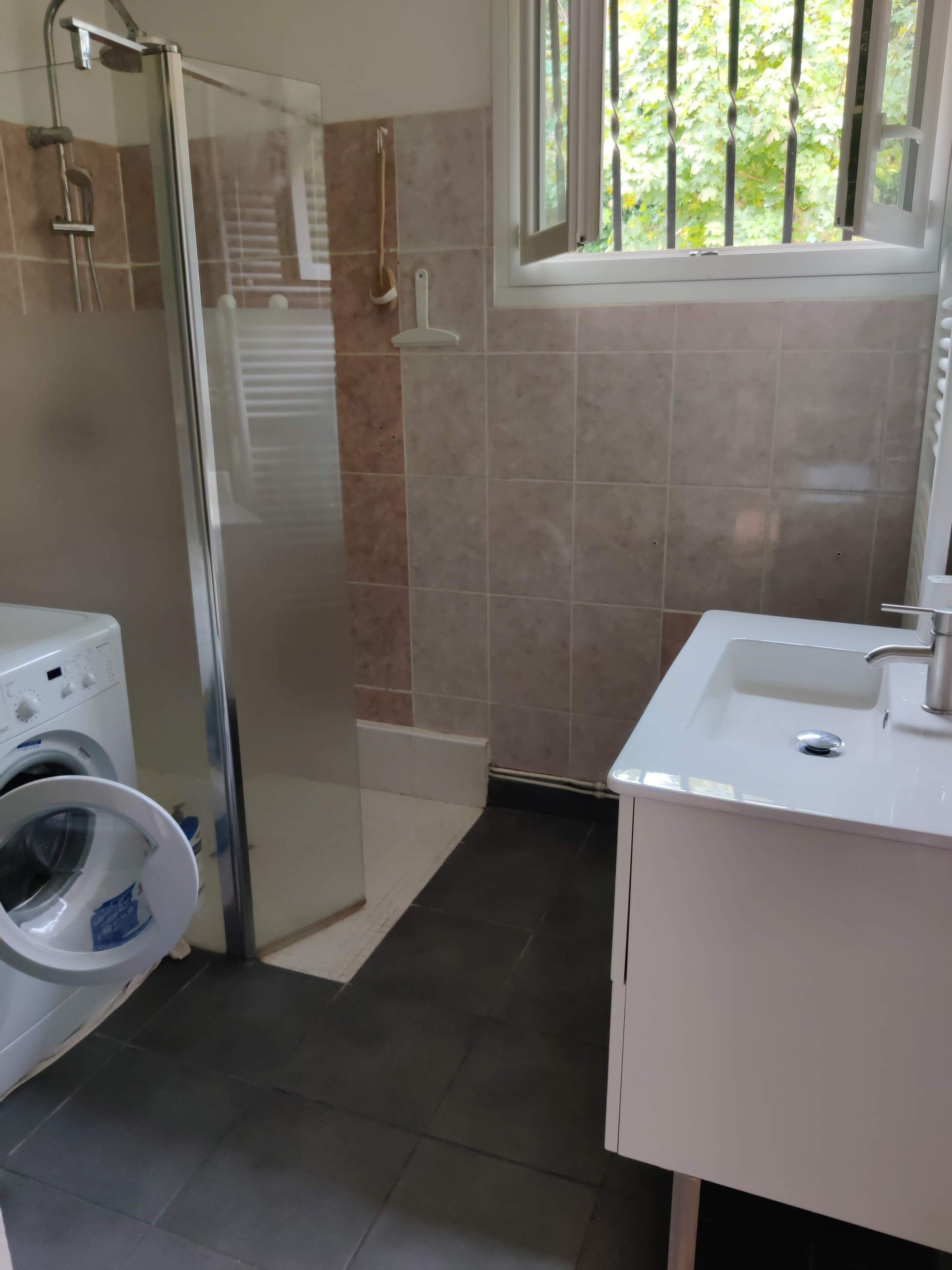 Une salle de bain avec une douche à parois de verre, un lave-linge et un lavabo.