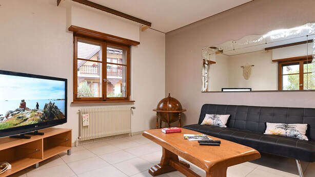 A living room with a television, a wooden coffee table, a black sofa, and a large mirror on the wall. - Charming Home Between Colmar and Mulhouse, Near Wine Route and Europa-Park, Sleeps 6 (Oberentzen)