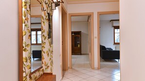 A spacious living area with a wooden bench, a large mirror with leaf-patterned wallpaper, and a view into another room through an open doorway. - Charming Home Between Colmar and Mulhouse, Near Wine Route and Europa-Park, Sleeps 6 (Oberentzen)