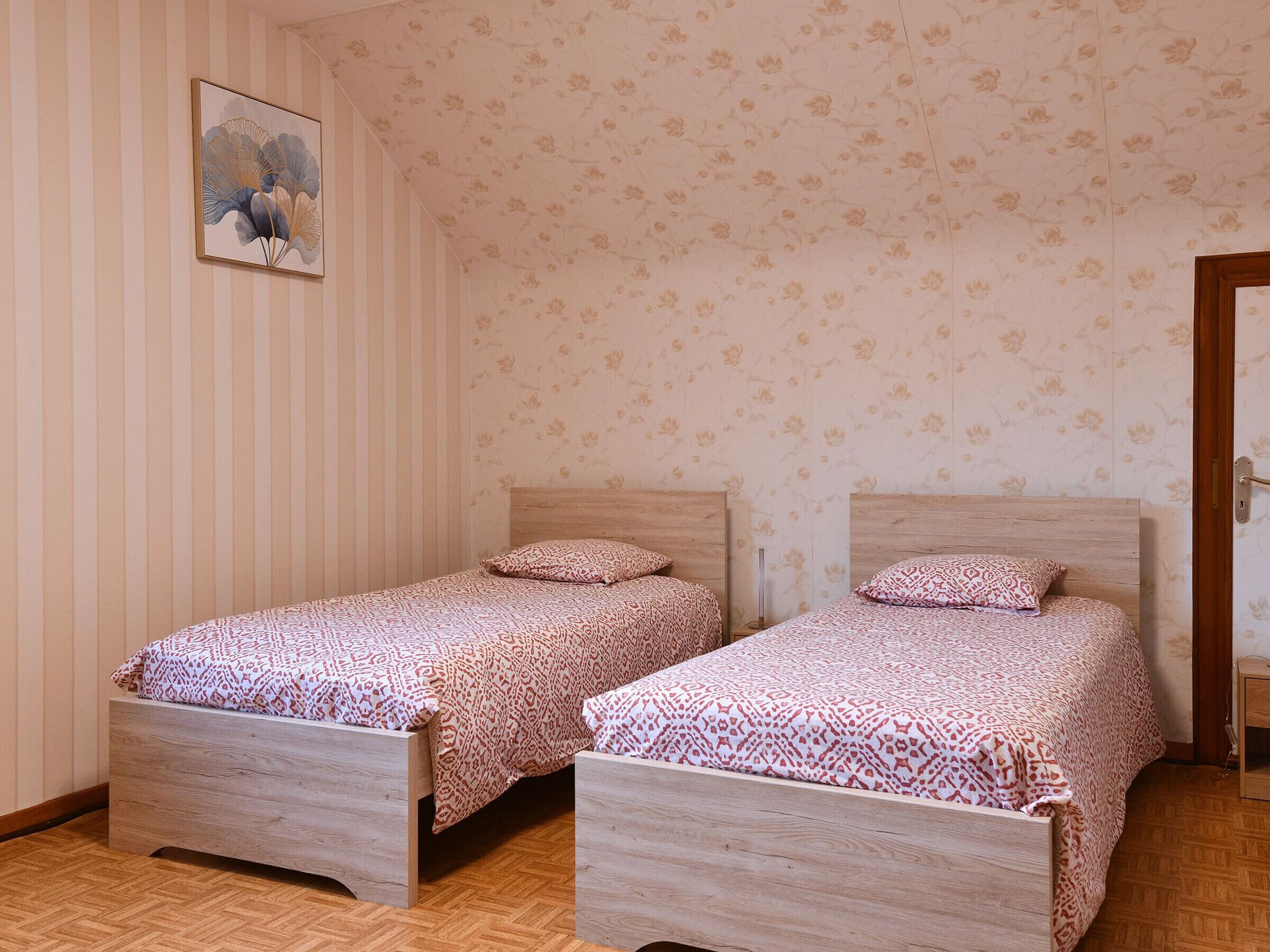 A room with two wooden beds, striped wallpaper, and a floral pattern on the walls.