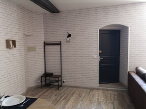 A room with white brick walls, a wooden floor, a black door, a small table with a chair, and a hanging light fixture.