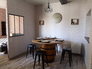 A dining area with a round wooden table, black stools, and a white brick wall.