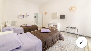 A hotel room with two beds, a desk, a chair, a TV, and a small shelf with decorative items.
