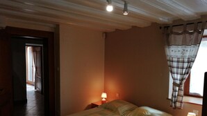 Un dormitorio con cama, dos lámparas de noche, una ventana con cortinas y una puerta que da a otra habitación.