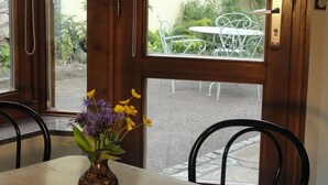 Una puerta de madera con un ventanal, una mesa y sillas de metal afuera, y un jarrón con flores sobre la mesa adentro.