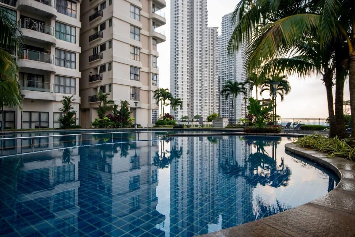 A swimming pool surrounded by high-rise buildings, palm trees, and a clear sky.