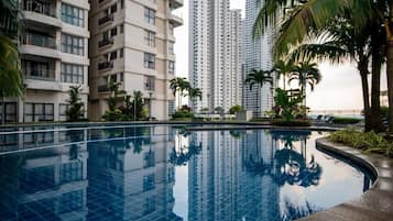A swimming pool surrounded by high-rise buildings, palm trees, and a clear sky.