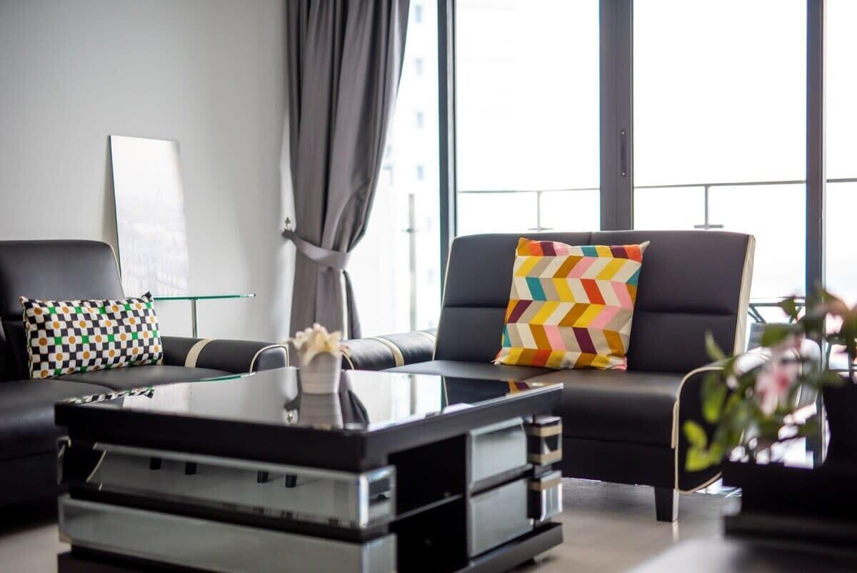 A modern living room with a black leather sofa, a glass coffee table, and a colorful chevron-patterned pillow.