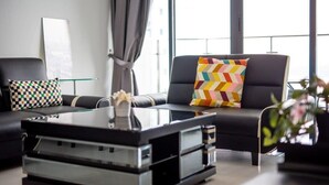 Ein modernes Wohnzimmer mit einem schwarzen Ledersofa, einem Glastisch und einem farbenfrohen Kissen mit Zickzackmuster.