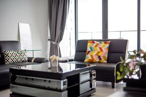 A modern living room with a black leather sofa, a glass coffee table, and a colorful chevron-patterned pillow.