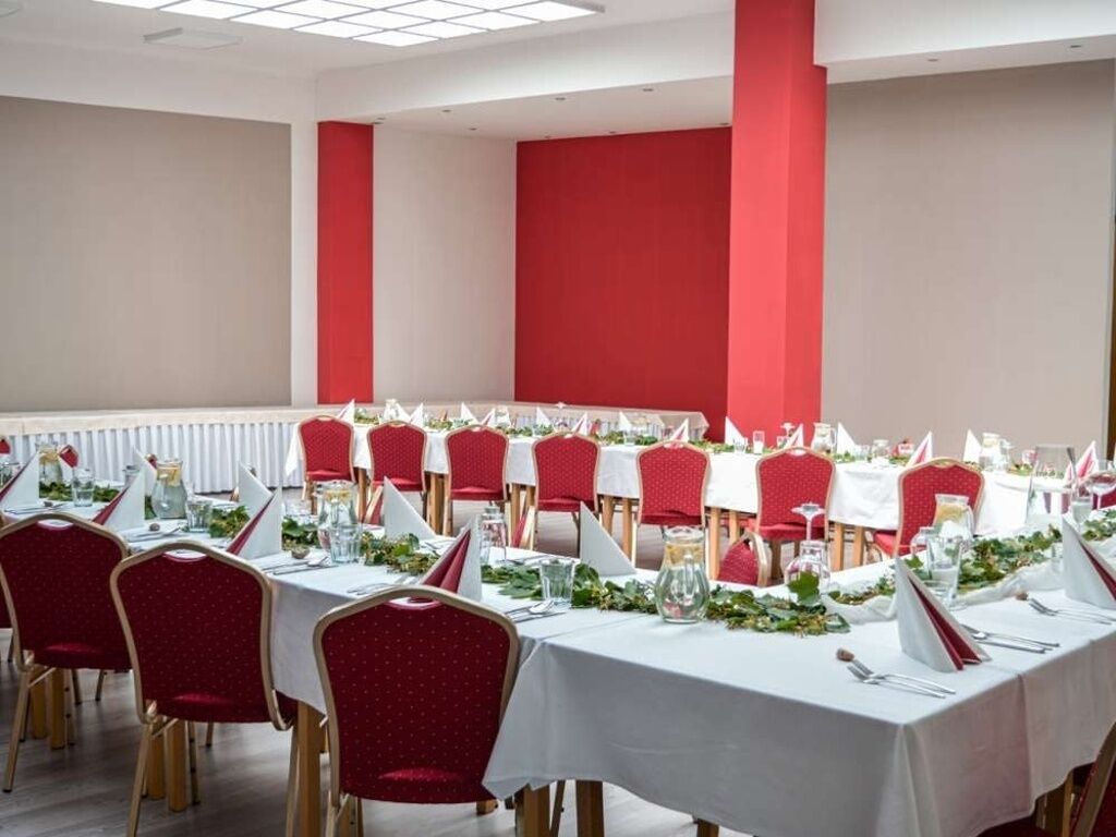A conference room with tables set for a formal event, featuring red chairs and white tablecloths.