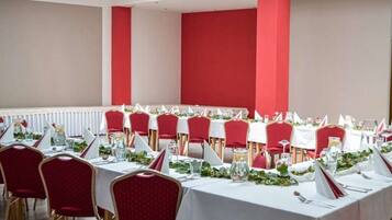 A conference room with tables set for a formal event, featuring red chairs and white tablecloths.