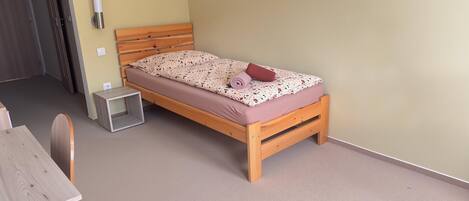 Un dormitorio pequeño y ordenado con una cama de madera, una mesita de noche y una silla.